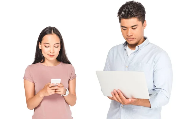 Красивая азиатская женщина, использующая смартфон рядом с парнем с ноутбуком изолированы на белом — стоковое фото