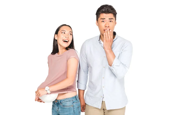 Scioccato asiatico uomo guardando fotocamera mentre fidanzata ottenere palla fuori di t-shirt isolato su bianco — Foto stock