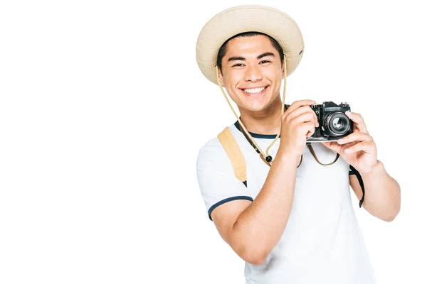 Happy asian tourist in hat holding digital camera and smiling at camera isolated on white — Stock Photo