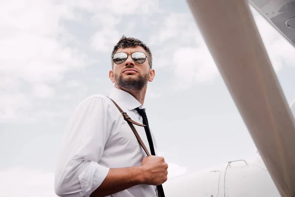 Bottom view of pensive pilot in sunglasses standing near plane — Stock Photo