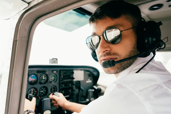 Pilot in sunglasses and headset looking at camera in plane — Stock Photo