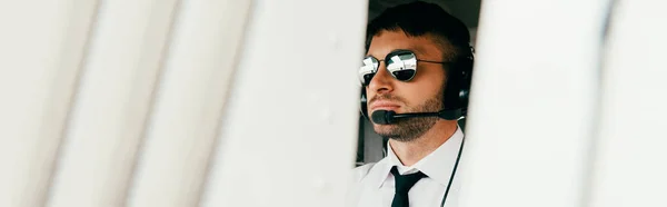 Панорамный снимок серьезного пилота в солнечных очках и гарнитуре, смотрящего в сторону — стоковое фото
