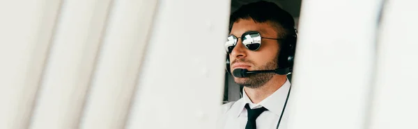 Plano panorámico de piloto serio en gafas de sol y auriculares mirando hacia otro lado - foto de stock