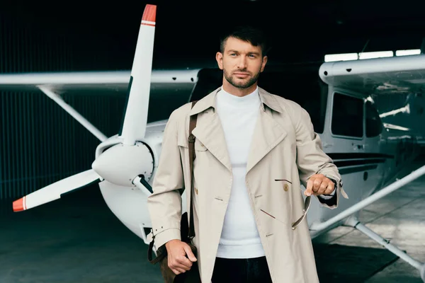 Pensive stylish businessman in coat standing near plane — Stock Photo