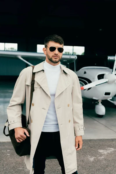 Pensativo hombre de negocios con estilo en abrigo de pie cerca de avión - foto de stock