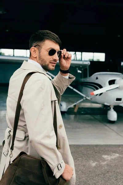 Pensativo hombre de negocios con estilo en abrigo de pie cerca de avión - foto de stock