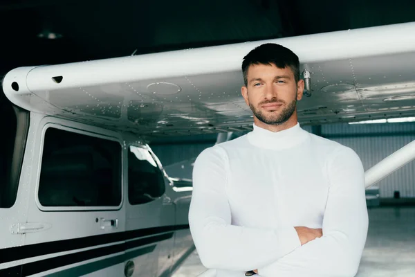 Joven guapo en traje casual de pie con los brazos cruzados cerca del avión - foto de stock