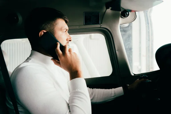 Side view of pilot talking on smartphone in plane — Stock Photo