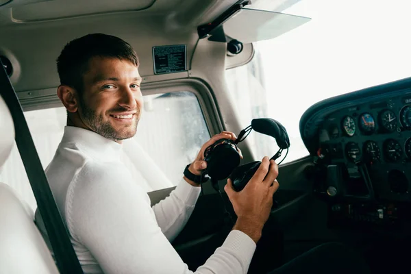 Souriant jeune homme barbu en tenue décontractée tenant des écouteurs dans l'avion — Photo de stock