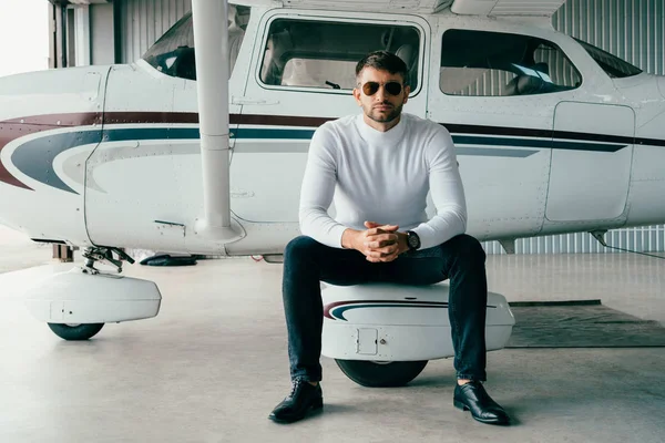 Panoramic shot of man in sunglasses and casual attire sitting with clenched hands near plane — Stock Photo