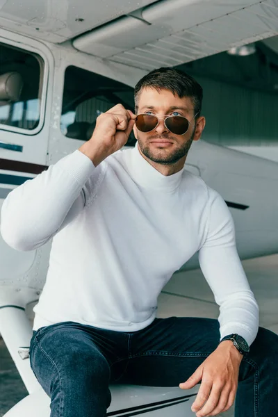 Hombre pensativo en gafas de sol y reloj de pulsera sentado cerca de avión — Stock Photo