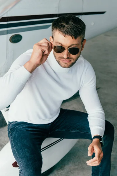 Uomo pensieroso in occhiali da sole e orologio da polso seduto vicino all'aereo — Foto stock