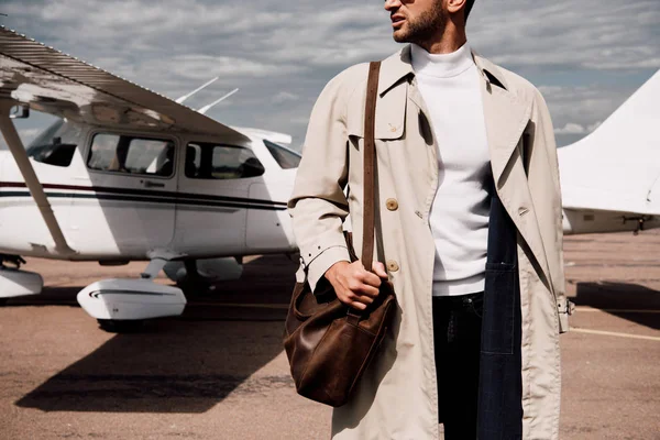 Vue partielle de l'homme en manteau debout près de l'avion par temps ensoleillé — Photo de stock