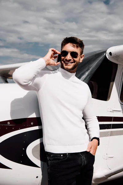 Smiling bearded man in sunglasses talking on smartphone near plane — Stock Photo