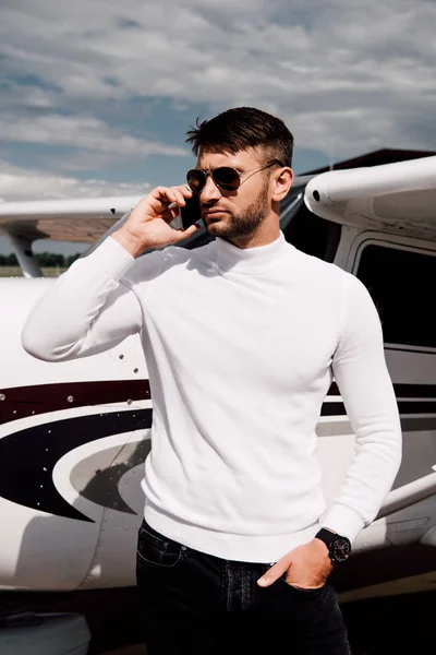 Hombre barbudo en gafas de sol hablando en smartphone cerca de avión - foto de stock