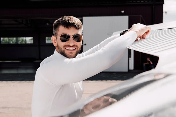 Homme barbu souriant dans des lunettes de soleil debout près de l'avion dans la journée ensoleillée — Photo de stock