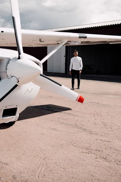 Vue pleine longueur de l'homme barbu dans des lunettes de soleil debout près de l'avion dans la journée ensoleillée — Photo de stock