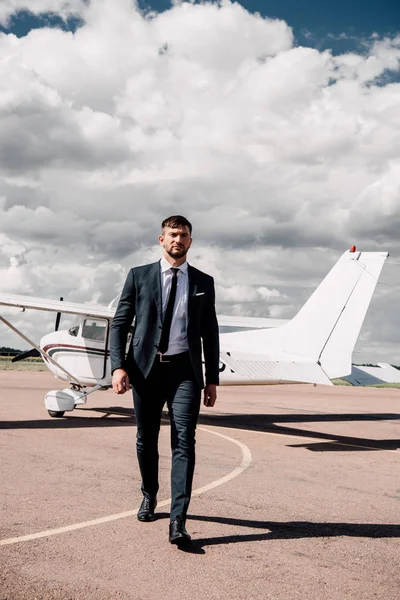 Vista completa de hombre de negocios en desgaste formal caminando cerca de avión - foto de stock