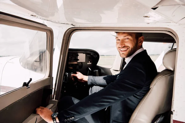 Усміхнений пілот в офіційному одязі сидить у літаку і тримає — стокове фото