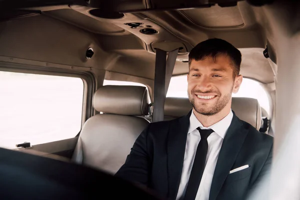 Smiling bearded pilot in formal wear sitting in plane — Stock Photo