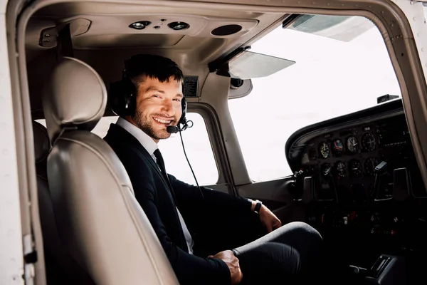 Sonriente piloto barbudo en traje formal sentado en avión - foto de stock