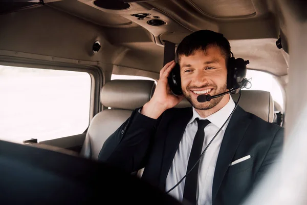 Улыбающийся бородатый пилот в формальной одежде и гарнитуре сидит в самолете — стоковое фото