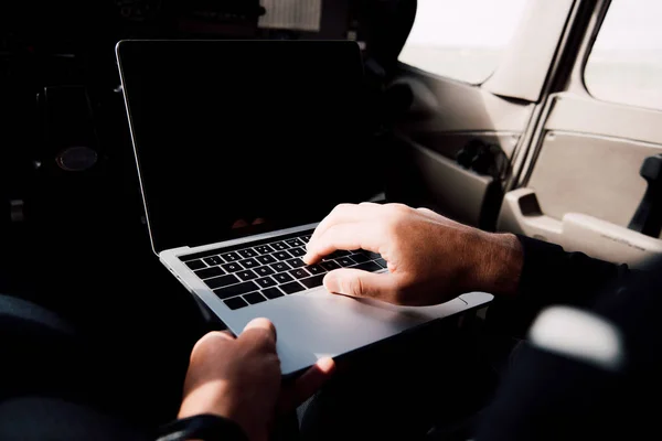Partial view of businessman in formal wear using laptop with blank screen in plane — Stock Photo