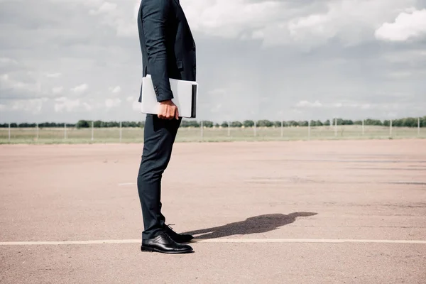 Частковий вид на бізнесмена в офіційному вбранні, що тримає ноутбук у сонячний день — стокове фото