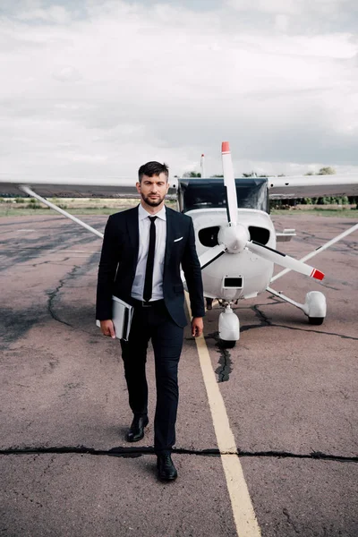 Vista completa di uomo d'affari in abbigliamento formale che tiene il computer portatile vicino all'aereo nella giornata di sole — Foto stock