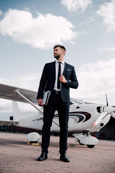 Повний погляд на бізнесмена в офіційному одязі, що тримає ноутбук біля літака в сонячний день — стокове фото