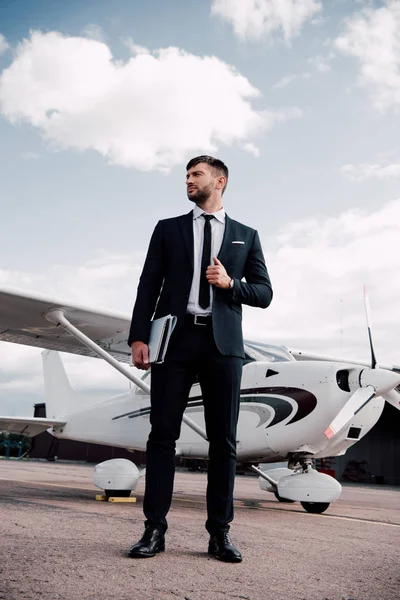 Vista completa de hombre de negocios en desgaste formal celebración de portátil cerca de avión en día soleado - foto de stock