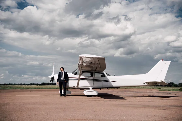 Vue pleine longueur de l'homme d'affaires en tenue formelle debout près de l'avion dans la journée ensoleillée — Photo de stock