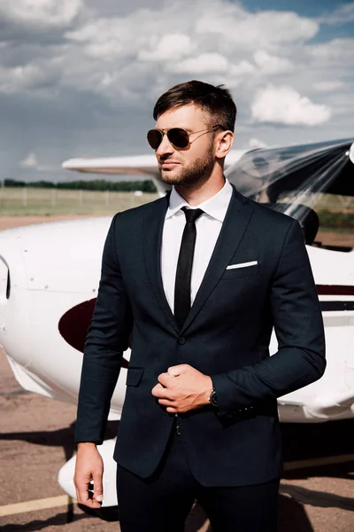 Задумчивый бизнесмен в формальной одежде стоит рядом с самолетом в солнечный день — стоковое фото