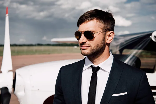 Pensive businessman in formal wear standing near plane in sunny day — Stock Photo