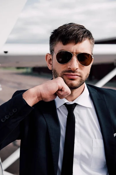 Задумчивый бизнесмен в формальной одежде стоит рядом с самолетом в солнечный день — стоковое фото