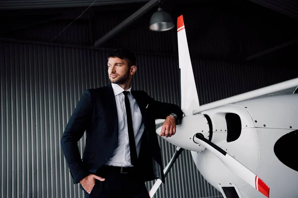 Confident businessman in formal wear standing with hand in pocket near plane — Stock Photo