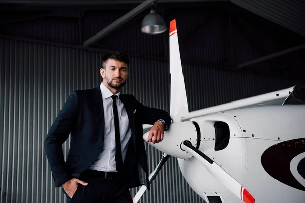 Confident businessman in formal wear standing with hand in pocket near plane — Stock Photo