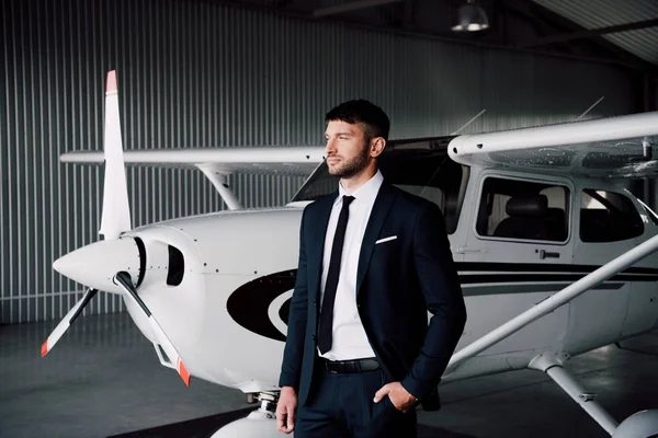 Homem de negócios confiante no desgaste formal de pé com a mão no bolso perto do avião — Fotografia de Stock