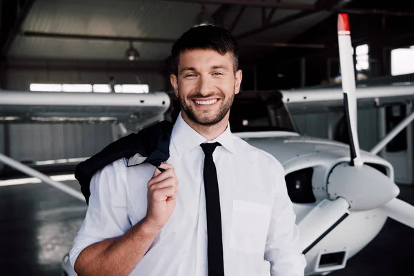 Piloto sorridente em desgaste formal de pé perto do avião e olhando para a câmera — Fotografia de Stock