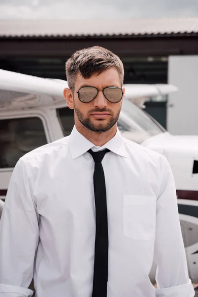 Pilote barbu confiant dans des lunettes de soleil debout près de l'avion — Photo de stock