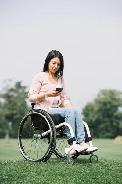 Mulher muito deficiente em cadeira de rodas usando smartphone enquanto descansa no parque — Fotografia de Stock
