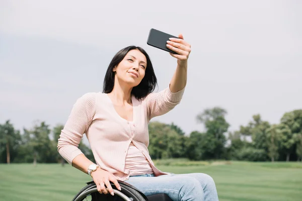 Femme handicapée gaie prenant selfie sur smartphone tout en marchant dans le parc — Photo de stock