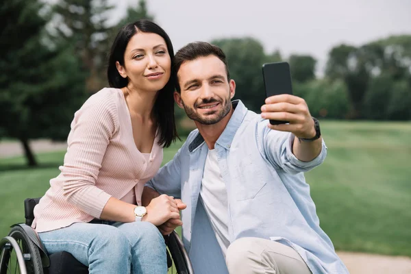 Glücklicher Mann macht Selfie auf Smartphone mit lächelnder behinderter Freundin im Park — Stockfoto
