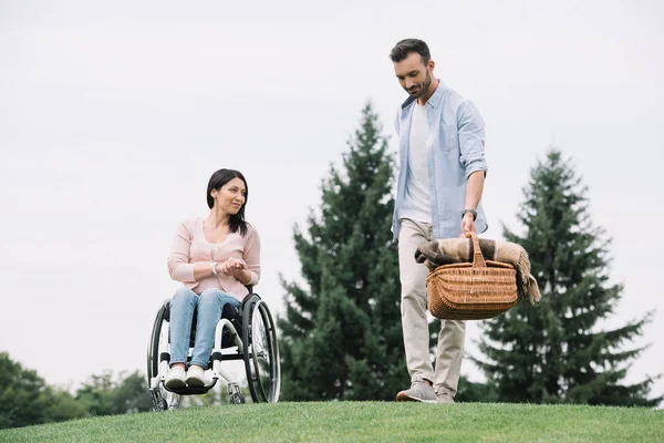 Handsome man holding straw basket near disabled girlfriend in park — Stock Photo