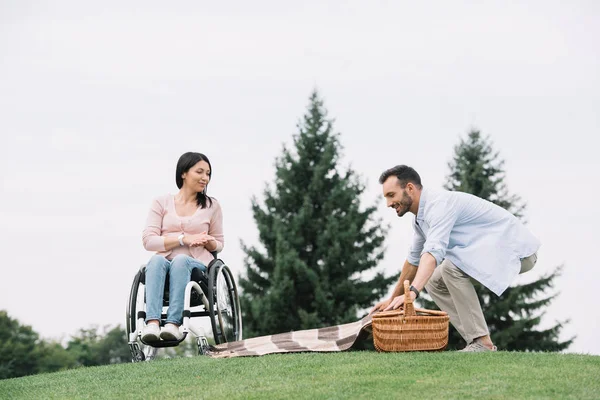 Happy man preparing place for picnic near disabled girlfriend in park — Stock Photo