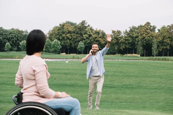 Homem feliz falando no smartphone e acenando mão para namorada com deficiência — Fotografia de Stock