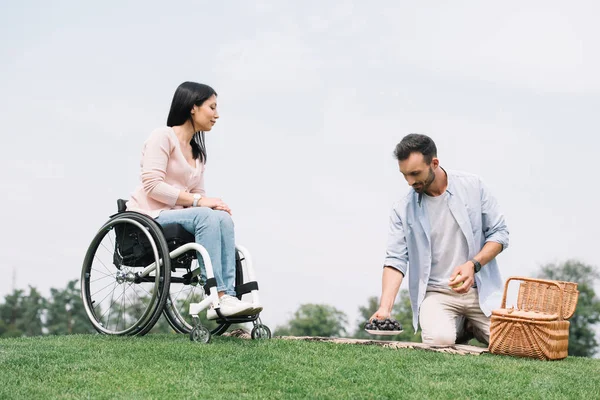 Handsome man holding plate with grape near disabled girlfriend in park — Stock Photo