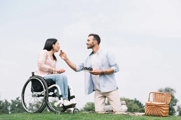 Happy man feeding disabled girlfriend with grape in park — Stock Photo