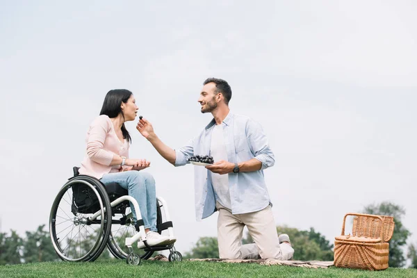 Heureux homme nourrir petite amie handicapée avec raisin dans le parc — Photo de stock