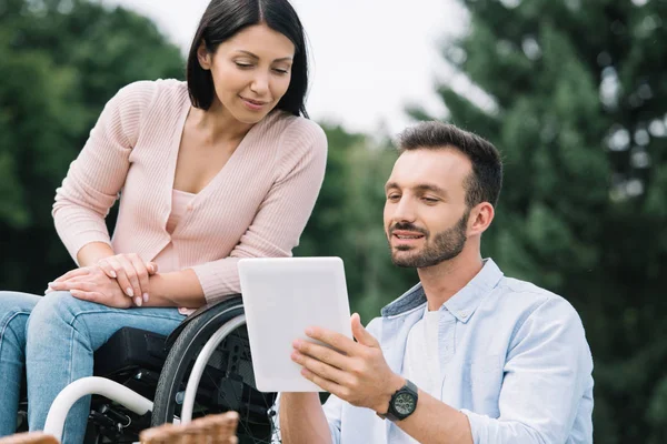 Щаслива жінка з інвалідністю і усміхнений хлопець, використовуючи цифровий планшет у парку — стокове фото